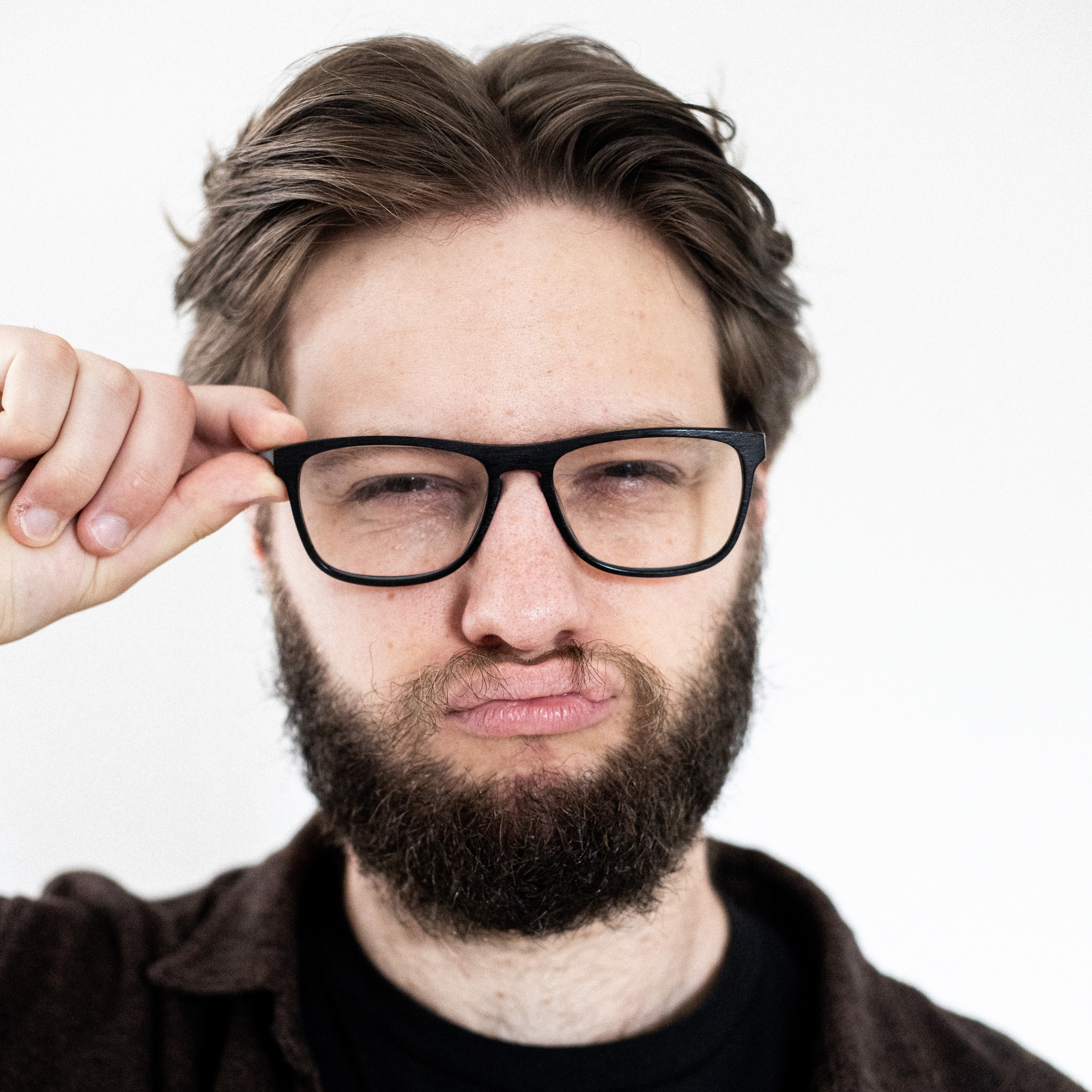 A close up photo of Luke pouting his lips and holding his glasses with one hand like a smart person.